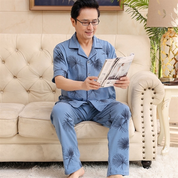 Bộ đồ ngủ nam trung niên màu xanh in họa tiết lá cọ ngồi đọc tạp chí trên ghế sofa