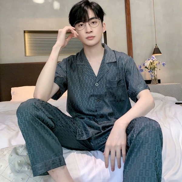 Nam giới mặc bộ pijama lụa màu xanh đậm họa tiết chữ G ngồi trên giường trong phòng ngủ hiện đại