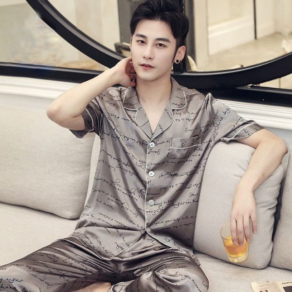 Bộ đồ ngủ lụa nam màu xám in chữ, cộc tay dài quần, người mẫu ngồi trên sofa cầm ly nước