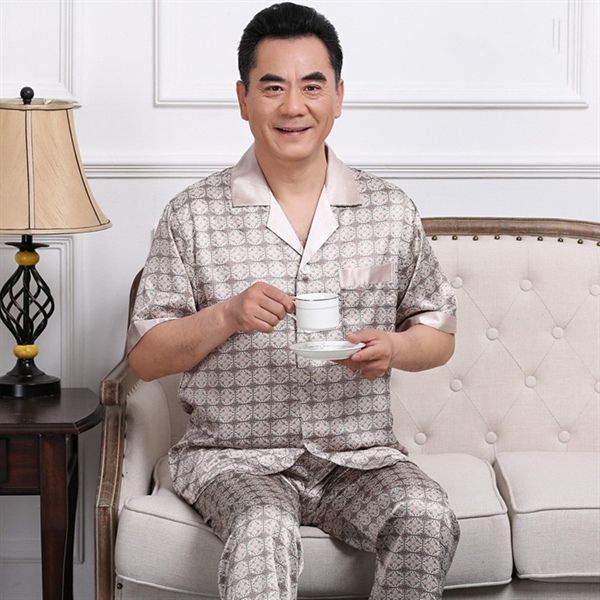 Bộ đồ ngủ lụa nam trung niên tay ngắn màu be họa tiết ngồi trên sofa cầm tách trà