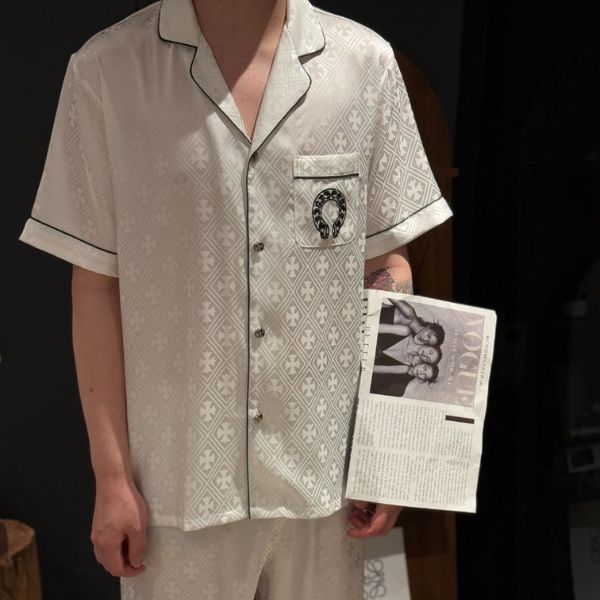 Bộ pijama lụa nam màu kem họa tiết caro nhỏ, viền đen, túi ngực in logo, người mẫu cầm tạp chí