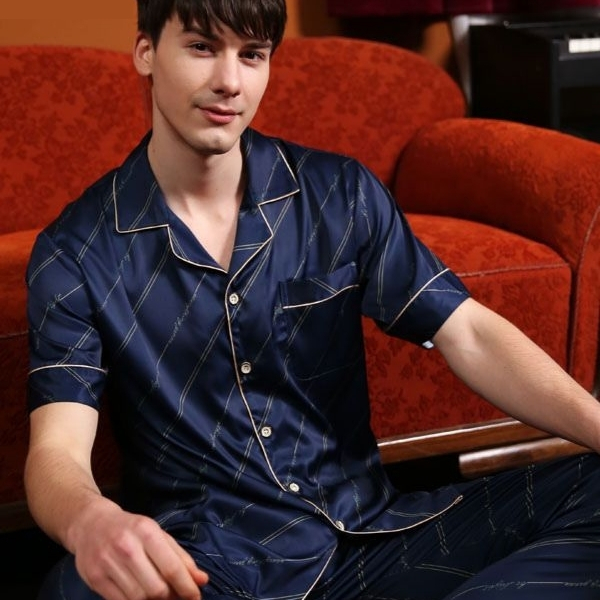 Nam giới mặc bộ pijama lụa màu xanh navy kẻ sọc ngồi trên ghế sofa đỏ