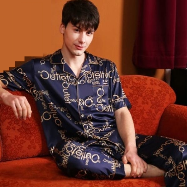Bộ pijama lụa nam màu xanh navy họa tiết chữ vàng, tay ngắn quần dài, người mẫu ngồi trên ghế sofa đỏ