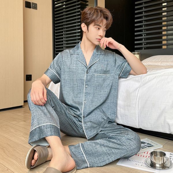 Bộ pijama nam màu xanh chất liệu mỏng nhẹ, tay ngắn quần dài, người mẫu ngồi cạnh giường ngủ