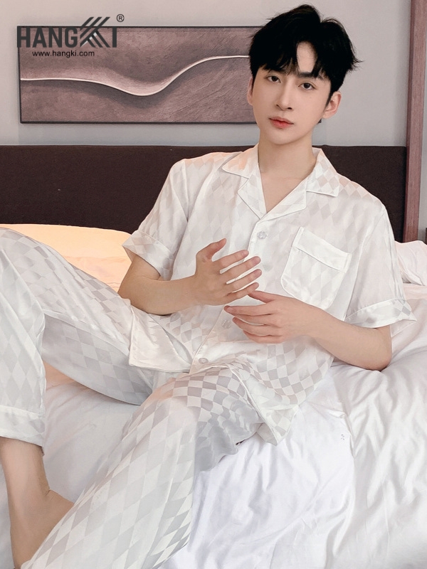 Nam giới mặc bộ pijama lụa trắng họa tiết caro thương hiệu Hangki ngồi trên giường