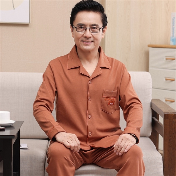 Bộ đồ ngủ nam trung niên màu nâu cam dài tay chất liệu mềm mại ngồi trên ghế sofa