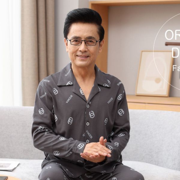 Bộ đồ ngủ nam trung niên màu xám họa tiết chữ ngồi trên ghế sofa trong phòng khách