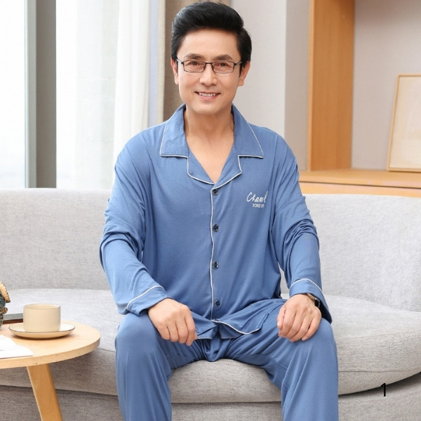 Bộ đồ ngủ nam trung niên màu xanh dài tay chất liệu mềm mại ngồi trên ghế sofa