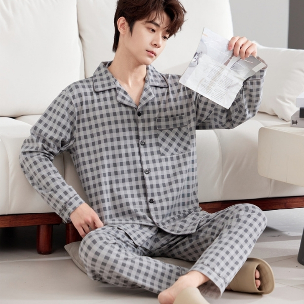 Nam giới mặc bộ pijama dài tay kẻ caro xám ngồi trên sàn cạnh sofa trong phòng khách