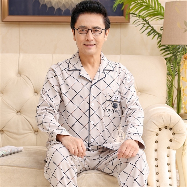 Bộ đồ ngủ nam trung niên màu be họa tiết caro ngồi trên ghế sofa trong phòng khách
