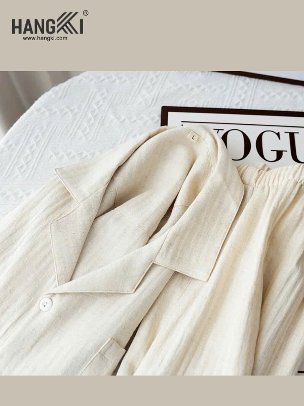 Bộ đồ ngủ lụa màu kem thương hiệu Hangki gồm áo cổ ve và quần cạp chun đặt trên giường