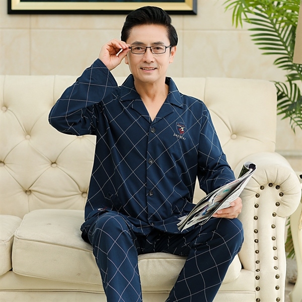Bộ pijama nam trung niên màu xanh đậm họa tiết caro ngồi trên sofa cầm tạp chí