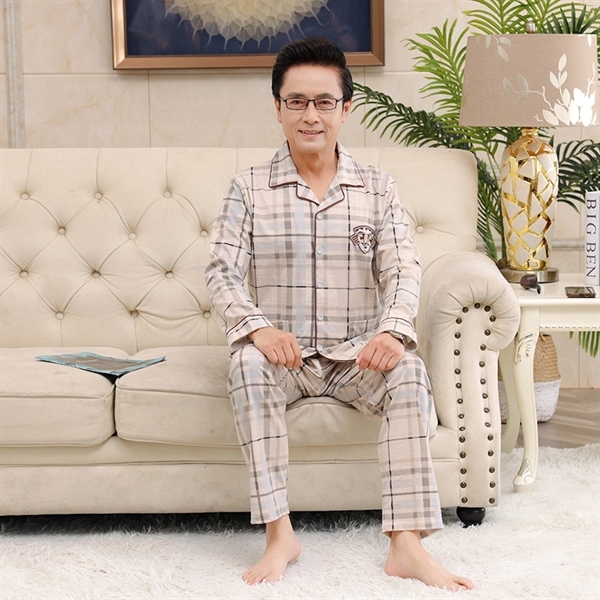 Bộ đồ ngủ nam trung niên kẻ caro dài tay quần dài màu be ngồi trên ghế sofa trong phòng khách