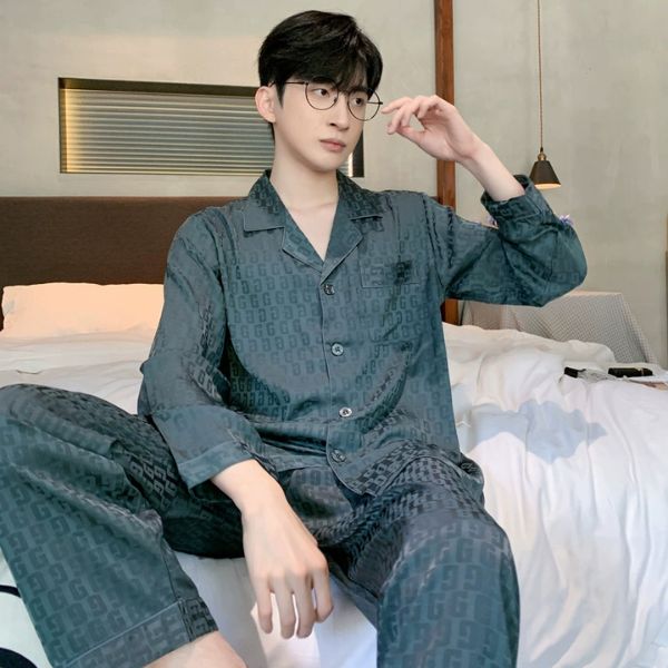 Nam giới mặc bộ pijama lụa màu xanh đậm họa tiết chữ G ngồi trên giường trong phòng ngủ