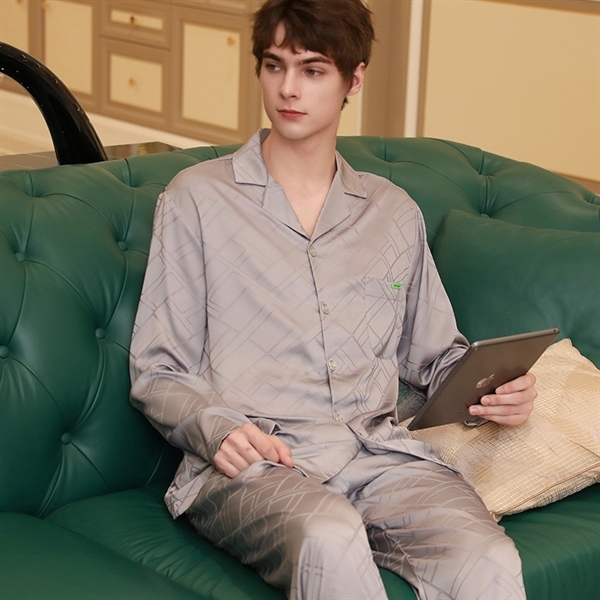 Nam giới mặc bộ pijama lụa màu xám dài tay quần dài ngồi trên sofa cầm máy tính bảng