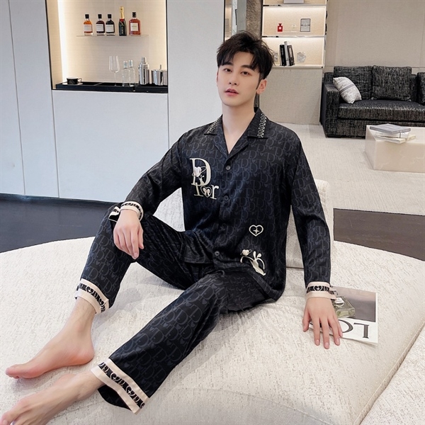 Nam giới mặc bộ đồ ngủ lụa màu đen họa tiết chữ Dior ngồi thư giãn trong phòng khách hiện đại