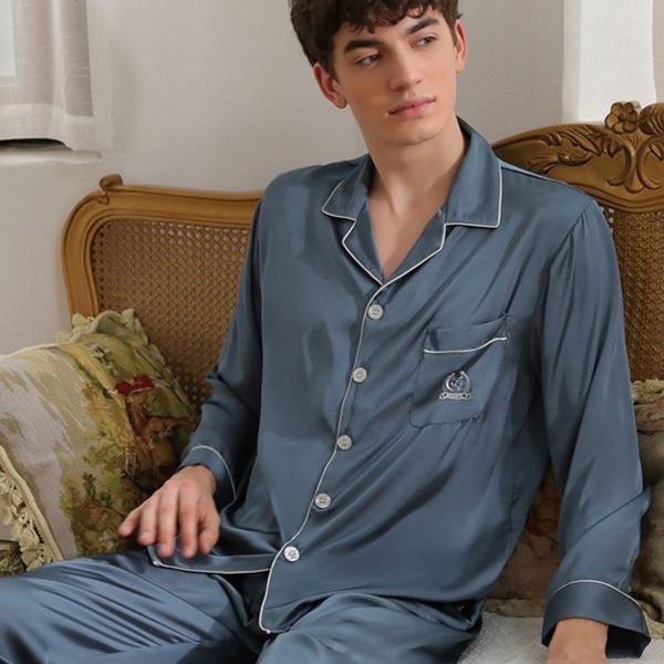 Bộ pijama lụa màu xanh cho nam với áo dài tay cổ bẻ và quần dài ngồi trên ghế sofa