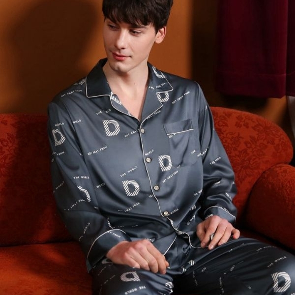 Bộ pijama lụa nam màu xanh đậm tay dài quần dài họa tiết chữ D ngồi trên ghế sofa đỏ