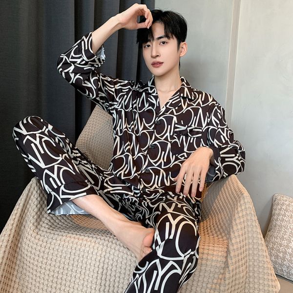 Nam giới mặc bộ pijama lụa đen họa tiết chữ trắng ngồi trên ghế trong phòng ngủ