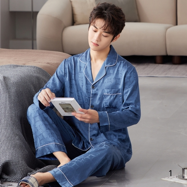Nam giới mặc bộ pijama lụa màu xanh ngồi trên sàn phòng ngủ, cầm sách đọc thư giãn