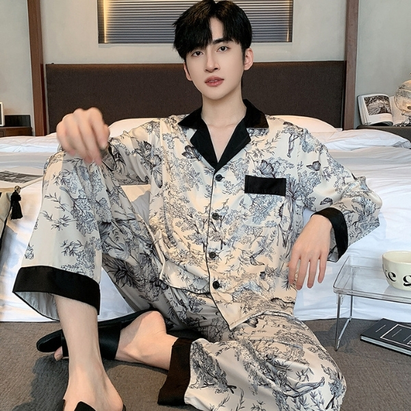 Nam giới mặc bộ pijama lụa dài tay họa tiết hoa lá màu be đen ngồi trên giường ngủ