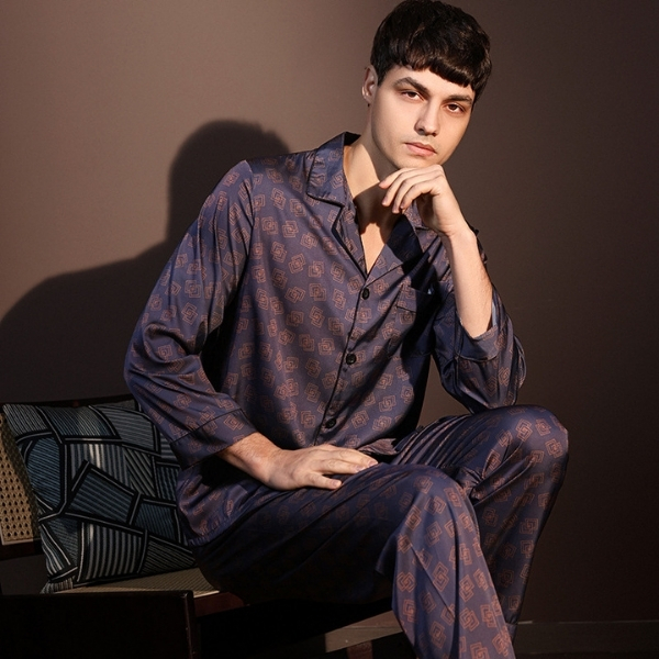 Nam người mẫu mặc bộ pijama lụa dài tay màu xanh họa tiết hình học ngồi trên ghế