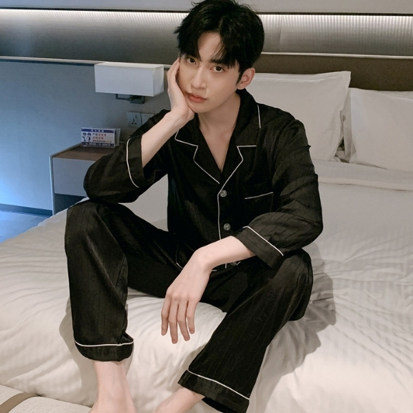 Nam giới mặc bộ pijama lụa màu đen viền trắng ngồi trên giường trong phòng ngủ hiện đại