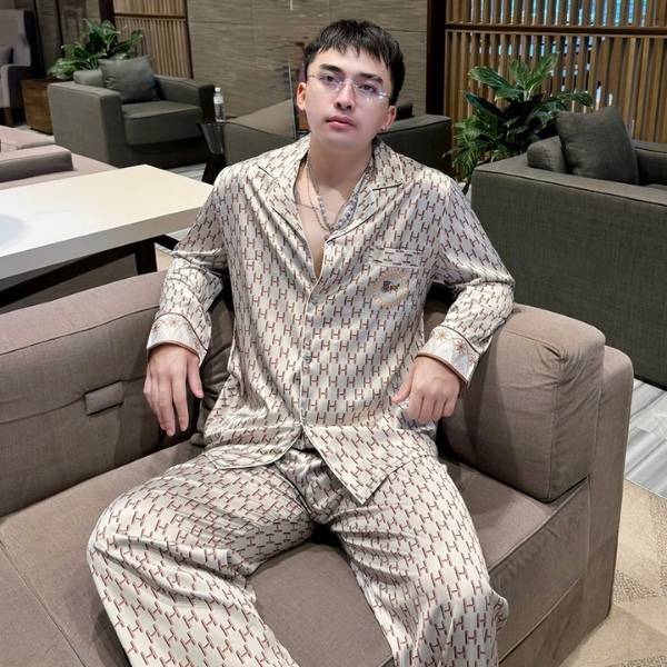 Bộ pijama lụa nam màu be họa tiết chữ H lặp lại, dáng rộng, người mẫu ngồi trên sofa trong phòng khách