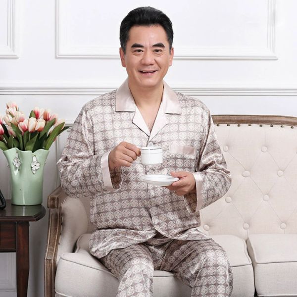 Bộ pijama lụa nam trung niên màu be họa tiết ngồi trên sofa cầm tách trà