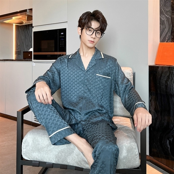Bộ pijama lụa nam màu xanh đậm họa tiết chìm, dáng dài tay quần dài, người mẫu ngồi trên ghế trong phòng khách
