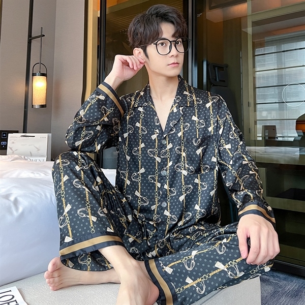 Nam giới mặc bộ pijama lụa dài tay họa tiết xích màu đen vàng ngồi trên giường trong phòng ngủ