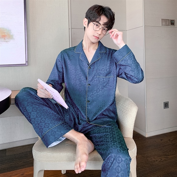 Nam giới mặc bộ pijama lụa màu xanh đậm họa tiết chữ ngồi trên ghế trong phòng ngủ