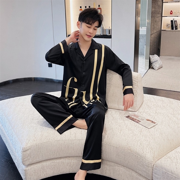 Bộ pijama lụa nam màu đen viền vàng dài tay quần dài, người mẫu ngồi trên sofa trong phòng khách hiện đại