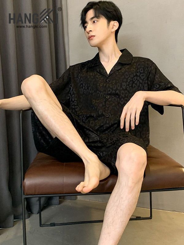 Nam người mẫu mặc bộ đồ ngủ lụa họa tiết da báo màu đen ngồi trên ghế da nâu