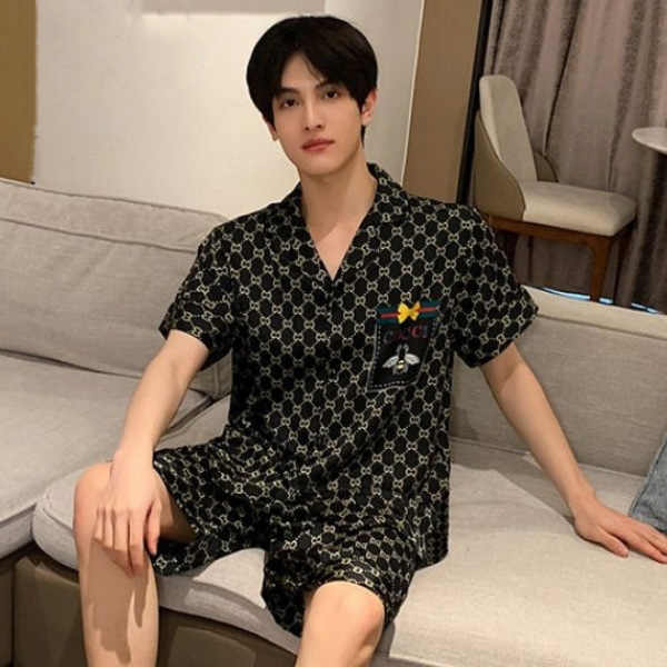 Chàng trai mặc bộ đồ ngủ nam họa tiết Gucci màu đen ngồi trên ghế sofa trong phòng khách