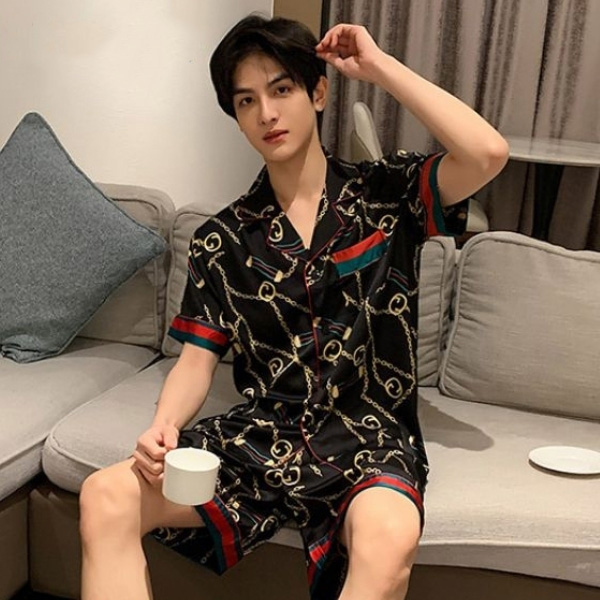 Bộ pijama nam lụa đen họa tiết xích vàng tay ngắn quần short ngồi trên sofa cầm cốc trắng