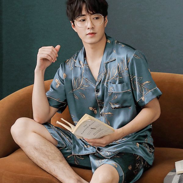 Nam giới mặc bộ pijama lụa xanh họa tiết lá ngồi trên ghế sofa cầm sách
