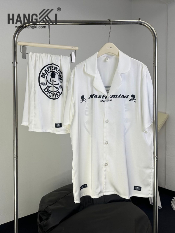 Bộ đồ ngủ lụa trắng Mastermind Dickies treo trên giá, gồm áo sơ mi cộc tay và quần short in logo